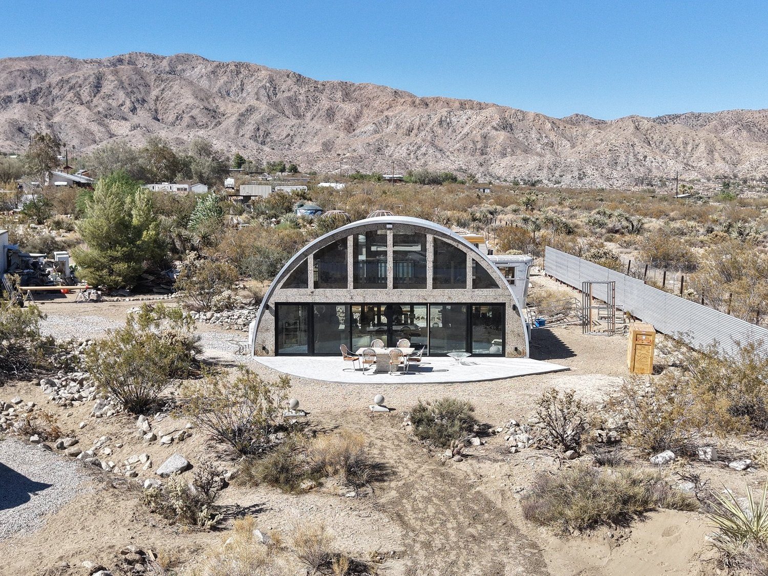 The arched glass front of the Center on its stone patio in open desert, rugged tan mountains rising behind