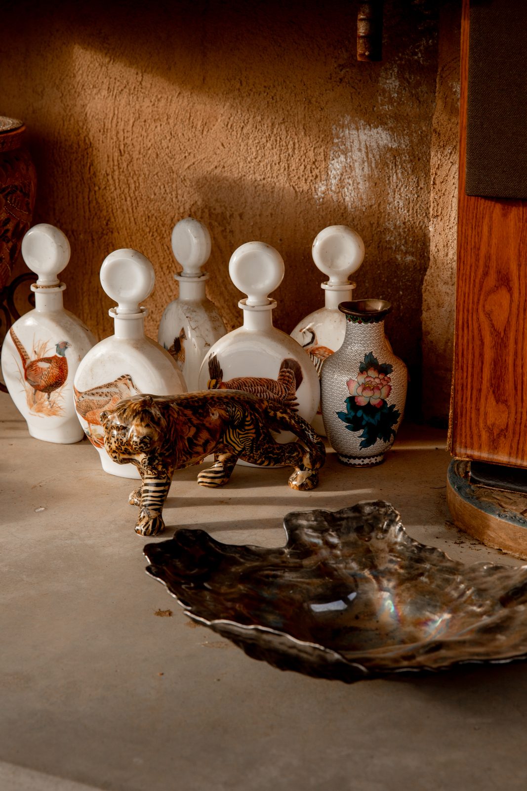 A shelf of sculpted figures and glass against a deep ochre wall