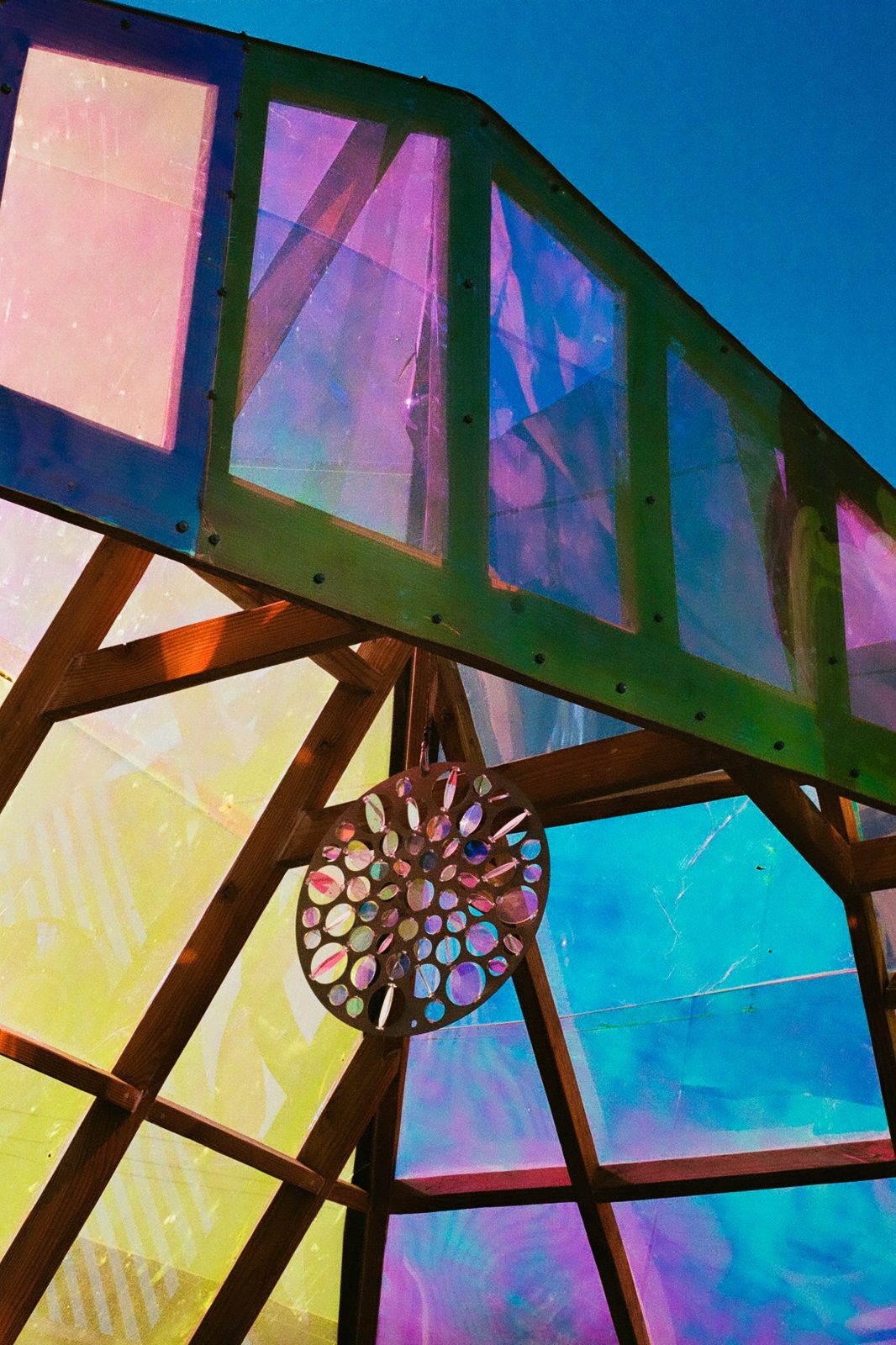 Iridescent glass panels in pink, violet, and gold above timber framing