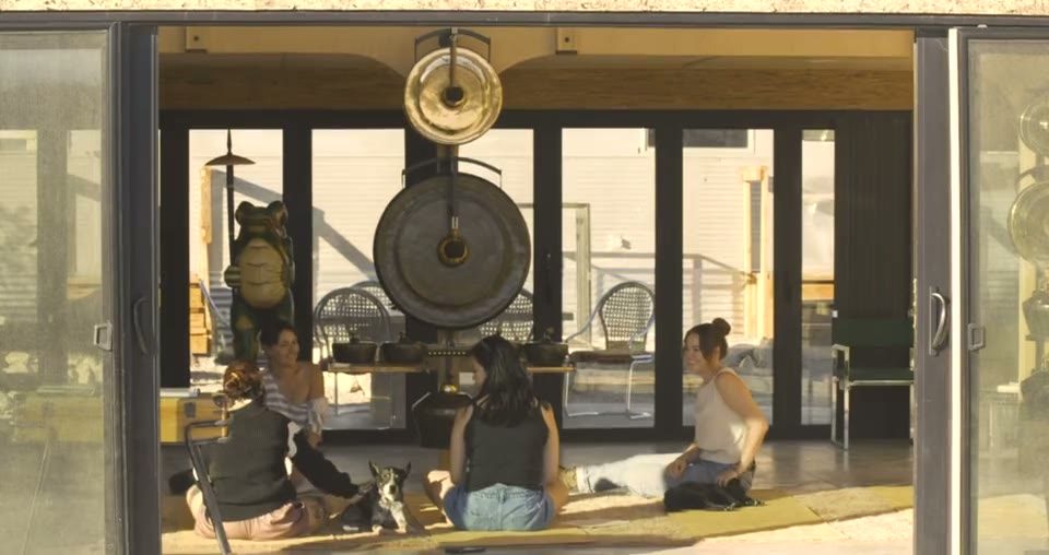 Three guests sitting on the floor of the Center beneath the Gamelatron's hanging bronze gongs